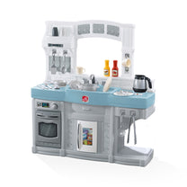 Step2 Choice Cuisine Kitchen — toy play kitchen with light blue counter, gray base, stovetop, oven, sink with faucet, pass-through arch, upper shelving, and 25+ accessories including toy food, pots, utensils, and coffeemaker; white background
