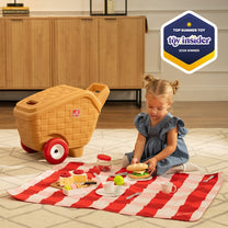 My First Picnic Basket — toddler girl in blue dress playing with toy picnic set on checkered blanket on rug; Top Summer Toy 2026 Toy Insider badge; picnic basket in background