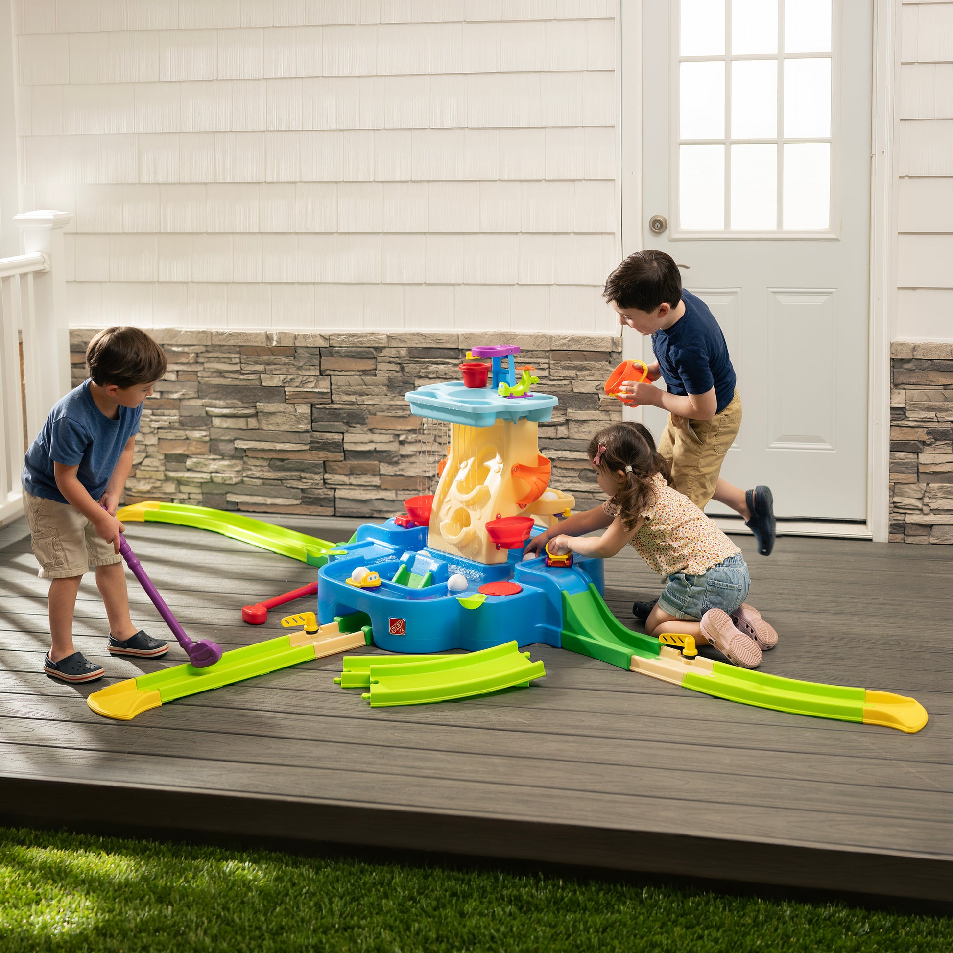 Putt-Splash Adventure Center — three children playing on outdoor deck; boy putting with purple putter along green fairway; girl kneeling at center base; older boy at right of tower; sunny setting