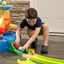 Putt-Splash Adventure Center — boy crouching indoors placing ball into green launch ramp at base of central tower; close-up of lower section and accessories