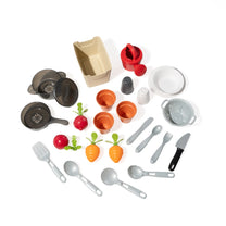 Garden Fresh Kitchen™ cookware and accessories flat lay on white background — tan produce crate, red watering can, salt shaker, pepper shaker, gray plate, gray colander, three terra cotta pots, gray Dutch oven with lid, gray skillet, spatula, spoon, ladle, play knife, two red radishes, two orange carrots, and gray fork