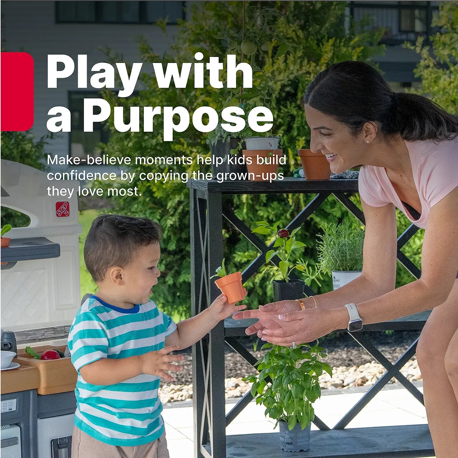 "Play with a Purpose" — Garden Fresh Kitchen™ being enjoyed by toddler boy in teal-striped shirt handing a small orange herb pot to his smiling mom on an outdoor patio; "Make-believe moments help kids build confidence by copying the grown-ups they love most"