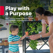 "Play with a Purpose" — Garden Fresh Kitchen™ being enjoyed by toddler boy in teal-striped shirt handing a small orange herb pot to his smiling mom on an outdoor patio; "Make-believe moments help kids build confidence by copying the grown-ups they love most"
