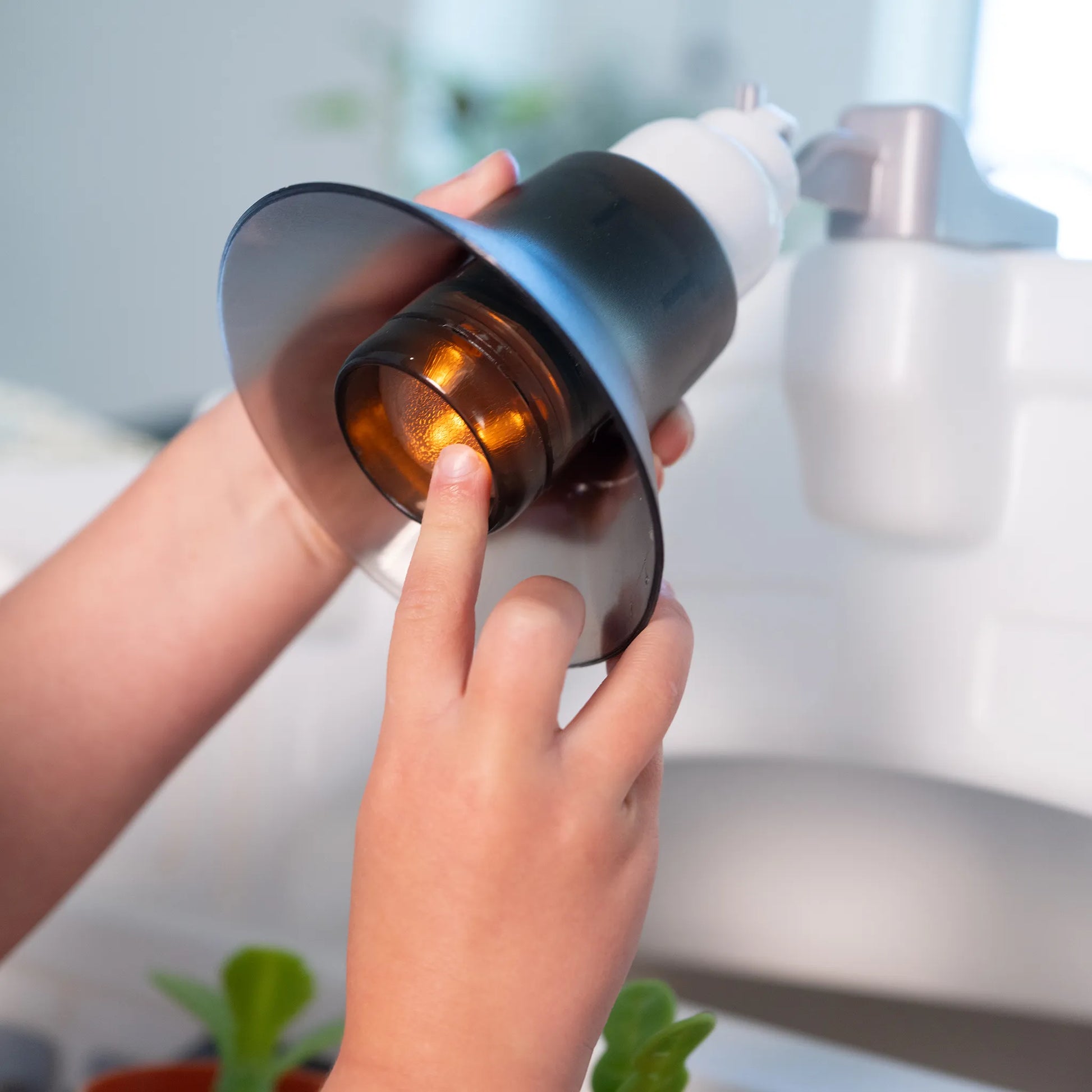 Close-up of child's hands pressing the working overhead pendant lamp button on the Garden Fresh Kitchen™; shows the black pendant lamp and sink/faucet area
