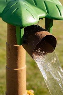Close-up of water streaming from the Tropical Splash Water Park™ palm tree's coconut-shell spout into the rock basin below