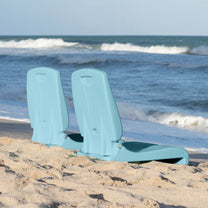 Two Flip Seat™ chairs in teal propped upright side by side in beach sand near the ocean shoreline