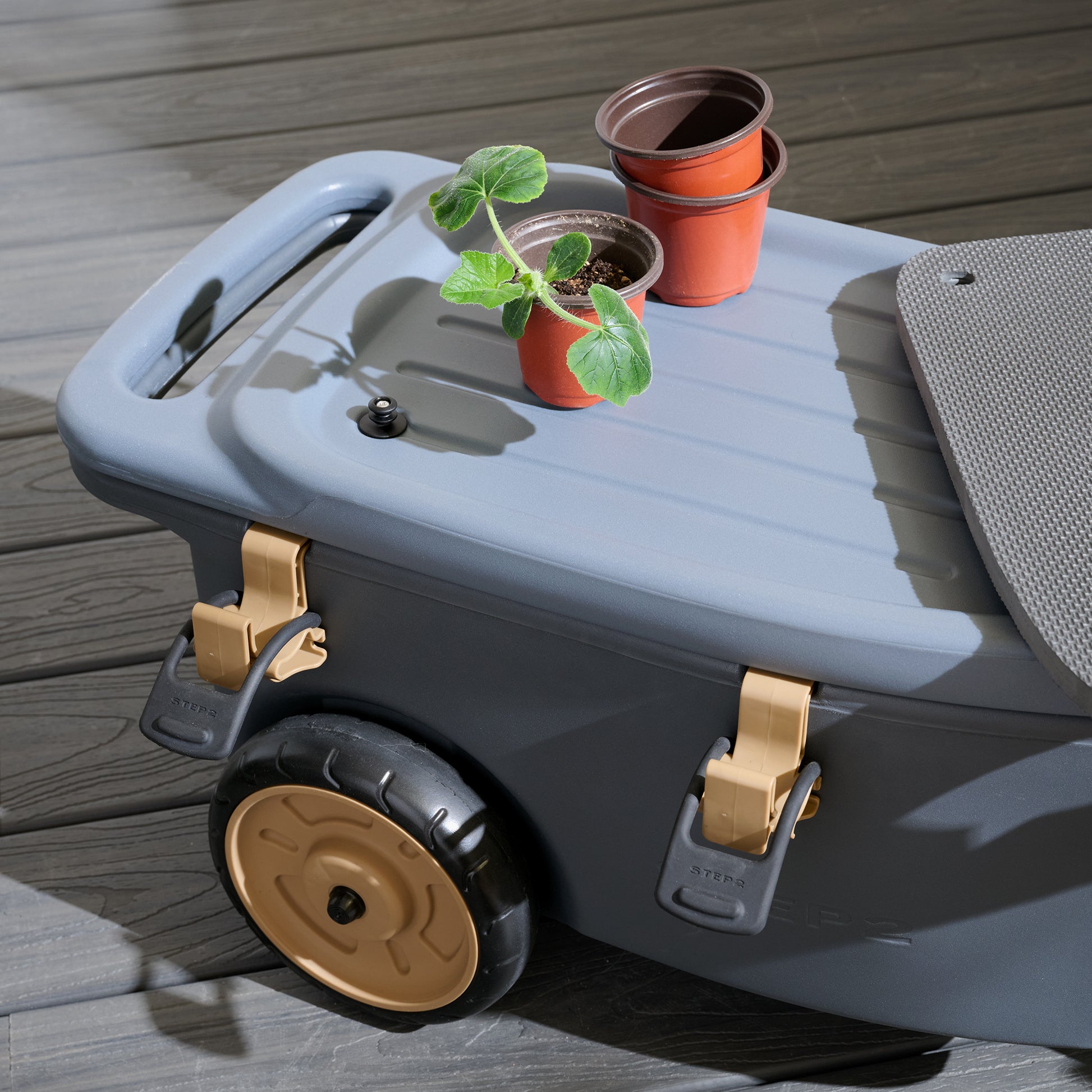 Top-down view of EverTough Garden Hopper on deck — lid open with seedling pots on surface, foam pad slid aside