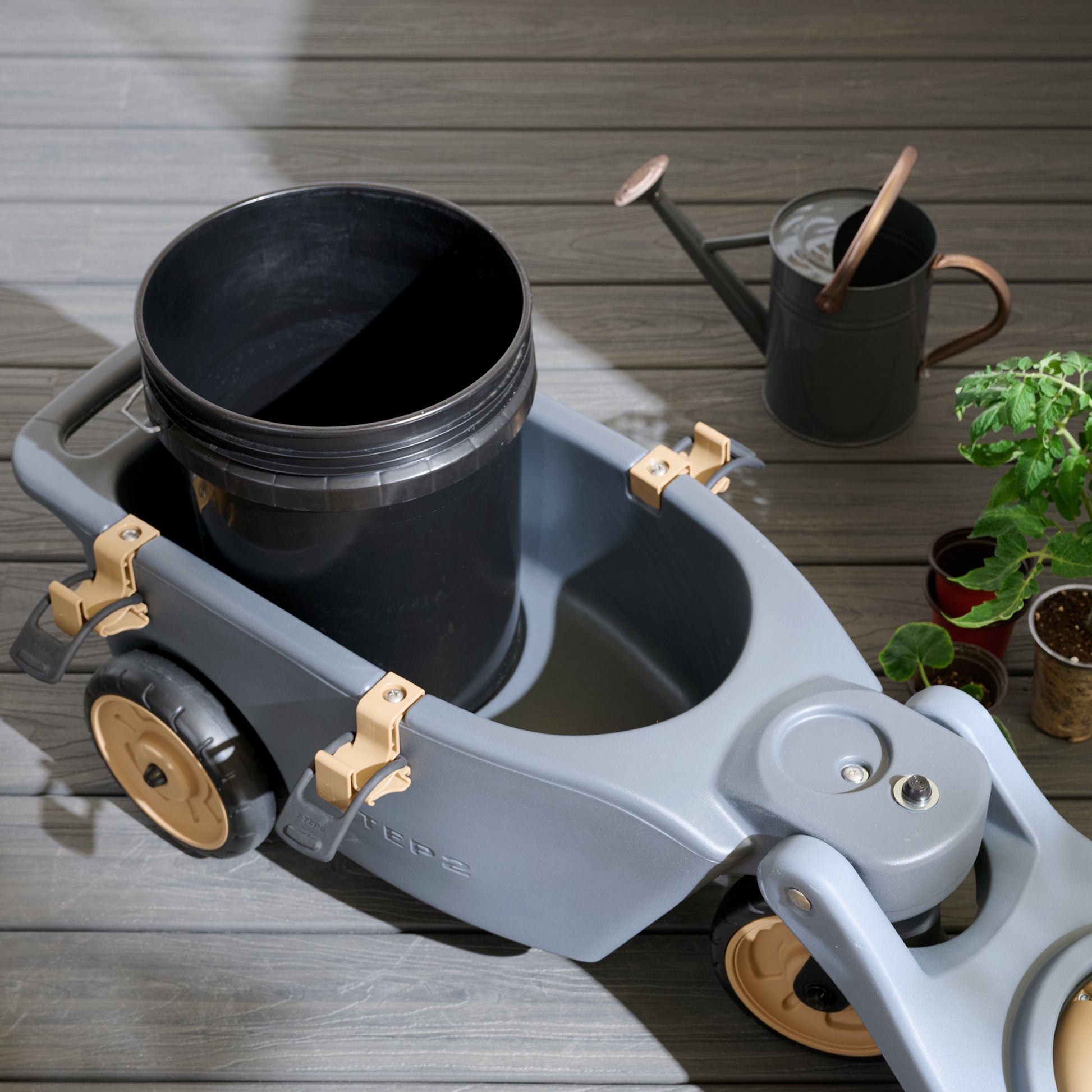 Top-down view of EverTough Garden Hopper — 5-gallon black bucket inside hopper basin with watering can and tomato plant nearby