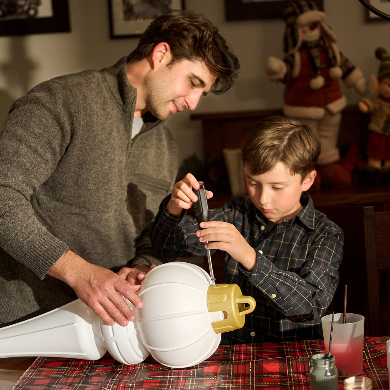 Paintable Large Outdoor Christmas Ornament being assembled by a father and son at a holiday table with a plaid tablecloth