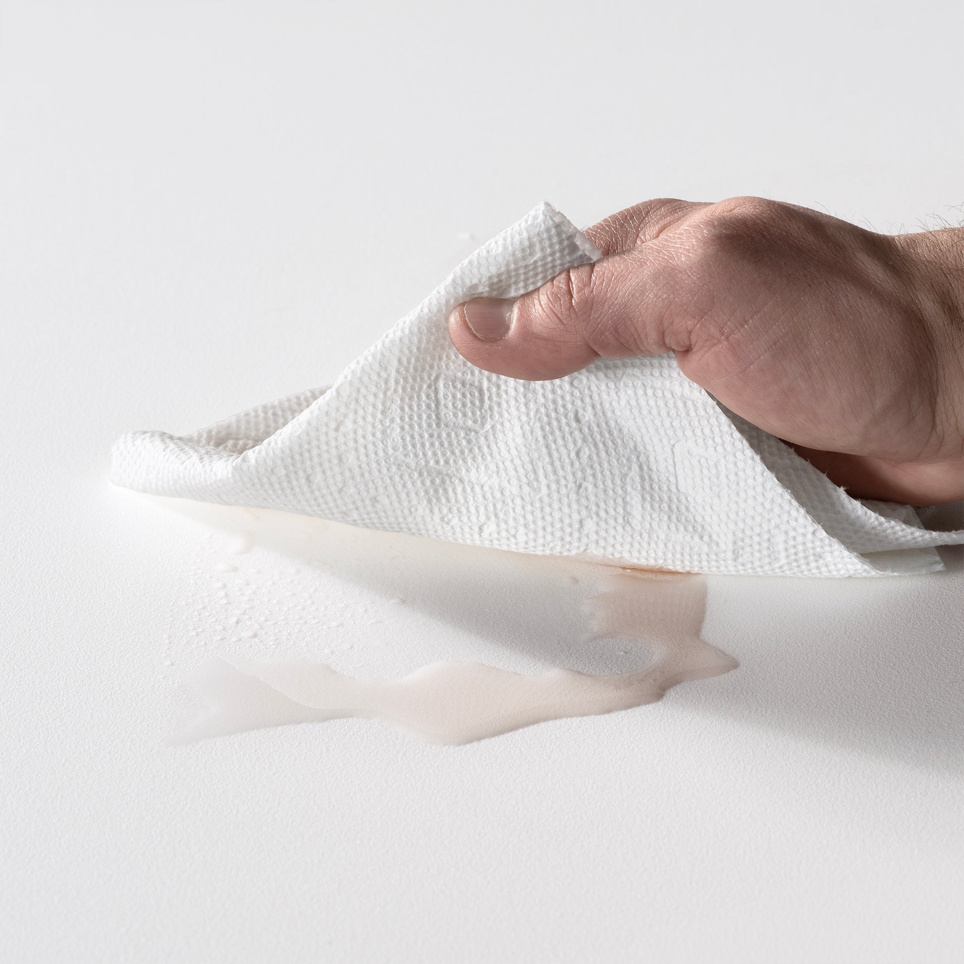 "Simple Setup, Easy Care" — hand wiping a spilled drink off the Vero In Pool Accent Table™ white matte surface with a paper towel; demonstrates the easy-clean durable material