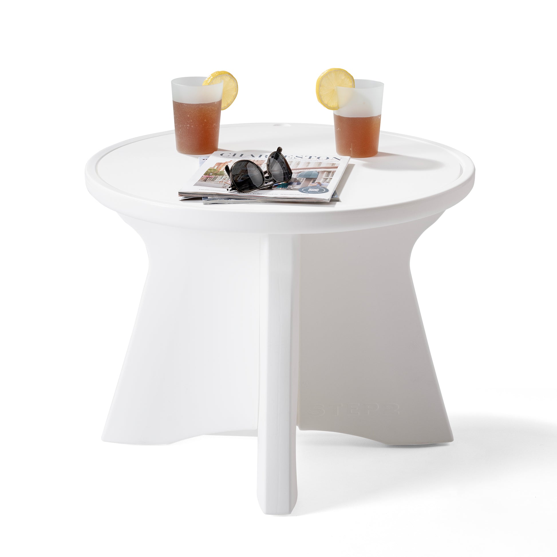 Vero In Pool Accent Table™ styled with two drinks with lemon slices, sunglasses, and a magazine on the round tabletop; shows built-in raised ring edge and four-panel base on white background