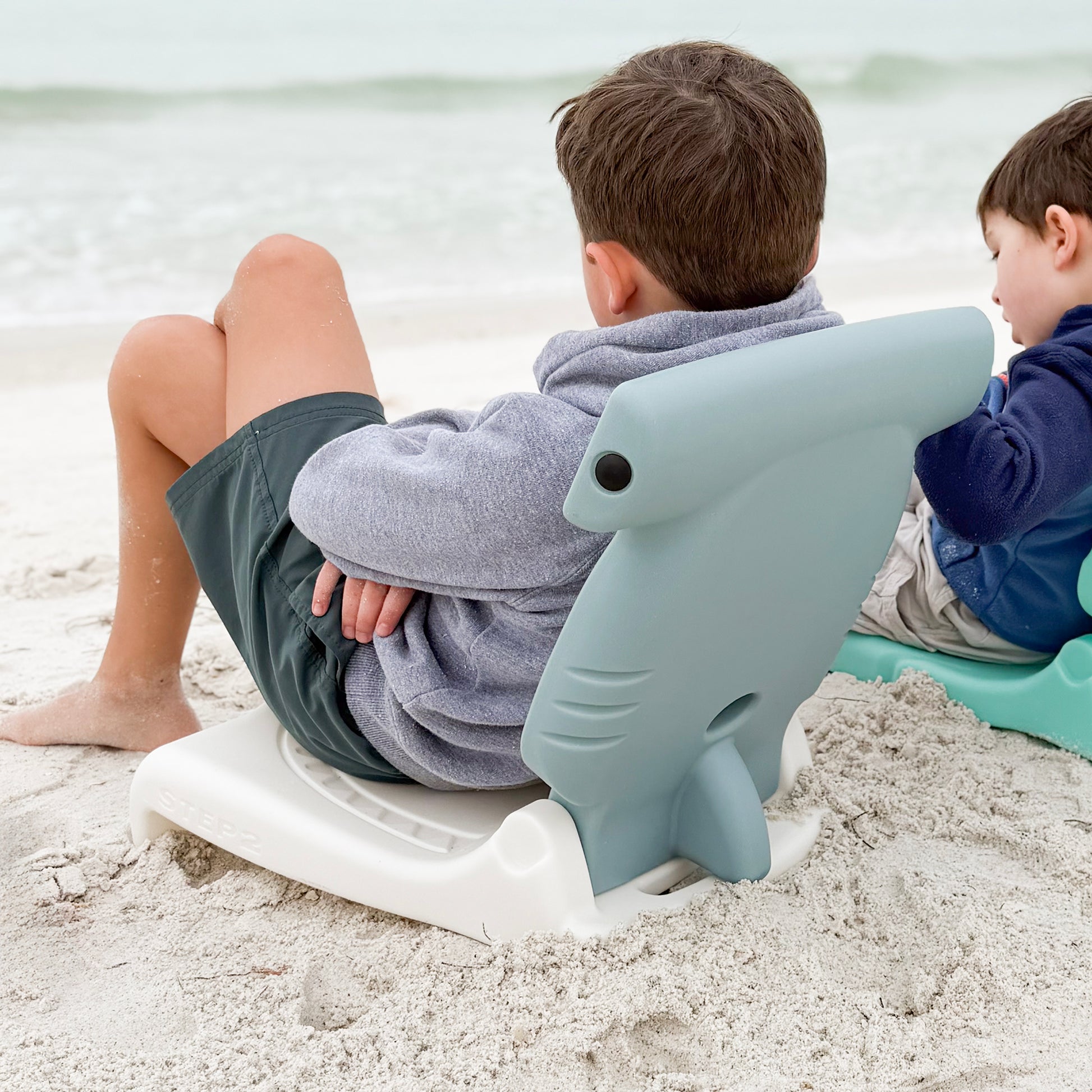 Step2 Kids Hammerhead Flip Seat — two boys on beach, older boy on gray hammerhead seat and younger boy on teal seashell seat, both looking at ocean