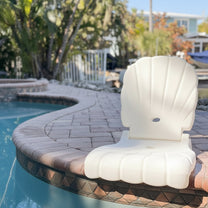 Step2 Seashell Flip Seat in white — upright on brick pool coping with tropical trees and pool water in background
