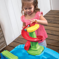 Close-up of toddler girl placing toy figure onto spiral water tower's yellow spinning platform