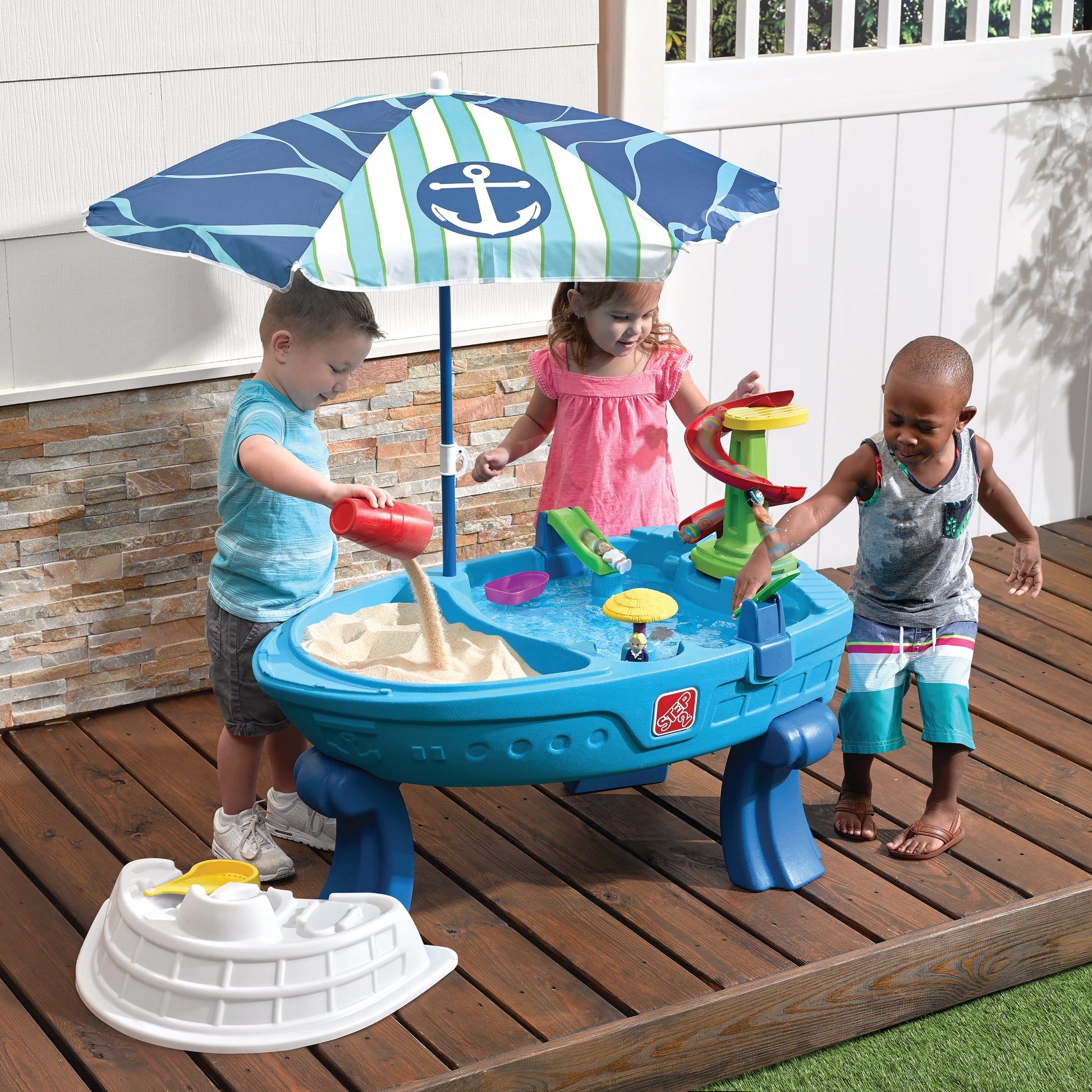 Three toddlers playing at Fiesta Cruise Water Table on wood deck — boy pouring sand, girl and boy at water section with spiral tower