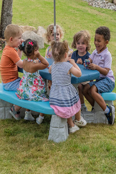 Children sitting around a blue playground table in a park