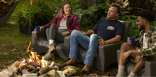 Three people sitting on a couch by a campfire in a natural setting