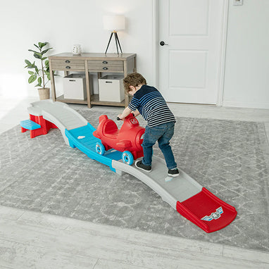 Child playing with a toy car track set on a rug in a room.