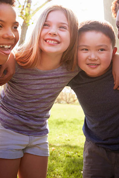 Three children hugging outdoors with a blurred background