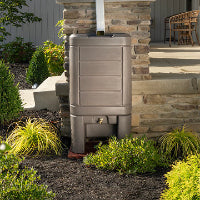 Rain barrel attached to a stone wall with plants around