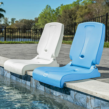 Two pool chairs, one white and one blue, on a pool ledge with a pool and trees in the background.