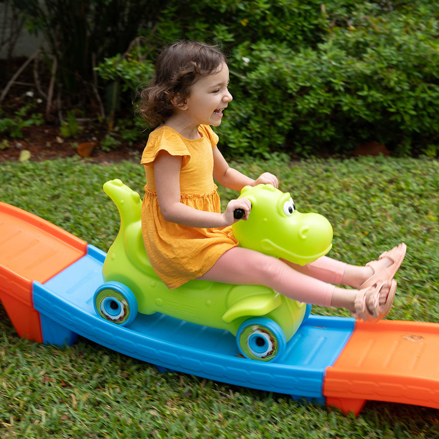 Child playing on a colorful toy slide with a green dinosaur-like figure outdoors.