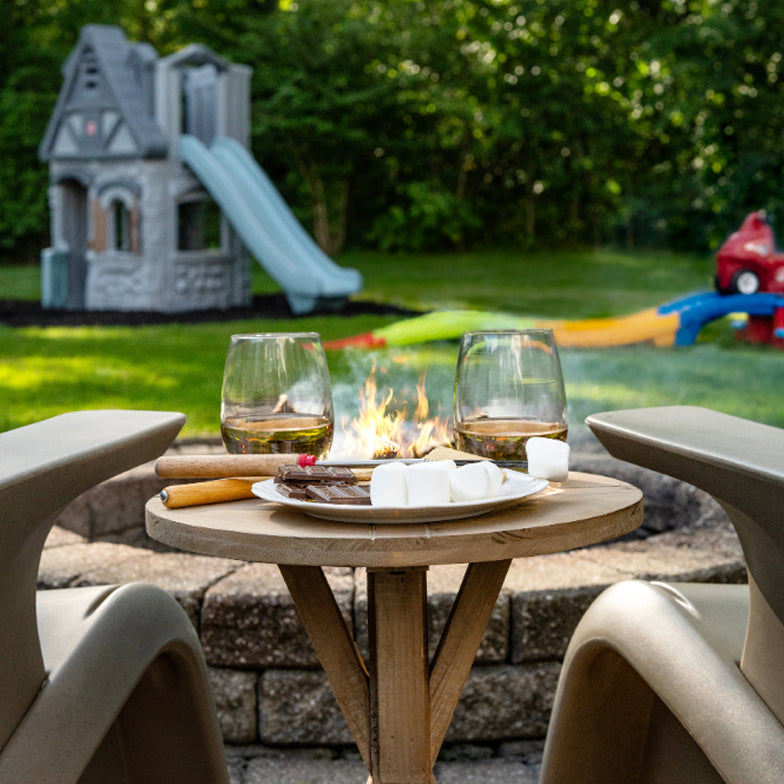 Outdoor setting with a fire pit table, chairs, and a playground in the background.