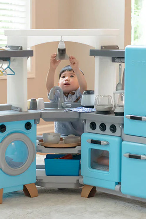 Child playing with a toy kitchen set in a room with light-colored walls.